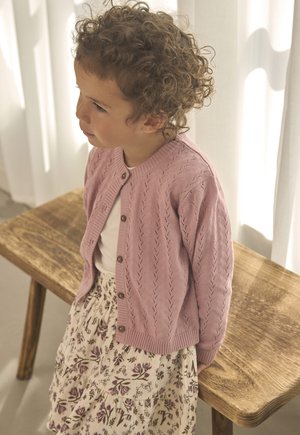 Cardigan rosa chiaro lavorato a maglia con motivo a diamante, scollatura rotonda e chiusura con bottoni, abbinato a una gonna a balze con stampa floreale.