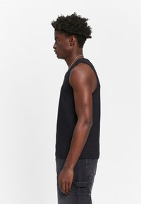 Black sleeveless tank top made from cotton, featuring a classic fit and smooth texture, paired with dark gray cargo pants.