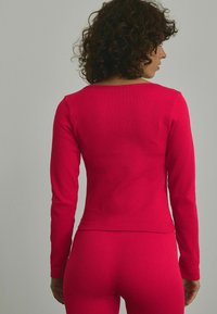Ribbet langærmet skjorte i lys pink, tætsiddende design med rund halsudskæring og smalle ærmer, der fremhæver en glat tekstur og subtil stræk.