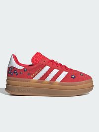 Baskets rouges Adidas Gazelle avec des rayures blanches, des fleurs bleues brodées et une semelle épaisse en gomme sur fond clair.