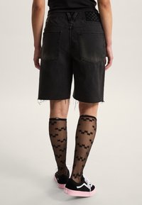 Pantalones cortos de mezclilla negra con dobladillo deshilachado, combinados con calcetines hasta la rodilla negros con estampado y zapatillas negras con suelas rosas.