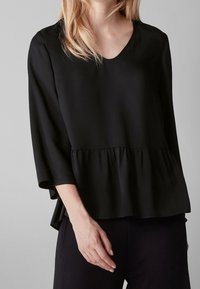 Schwarze Bluse mit V-Ausschnitt, Dreiviertelärmeln und einem Peplum-Saum. Glatter Stoff, lockere Passform und subtile Drapierungsdetails.