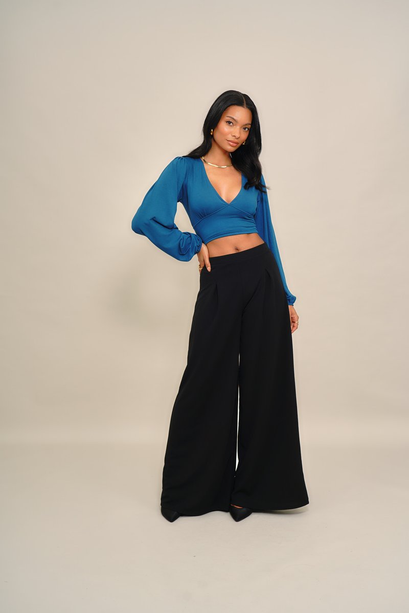 Tengeri kék rövid felső puffos ujjakkal és mély V-nyakkivágással, fekete, bőszárú nadrággal párosítva. Sima, enyhén fényes anyag.