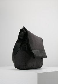 Borsa a tracolla nera con corpo in tessuto a trama, dettagli neri lisci, tracolla regolabile e chiusura a patta con logo.