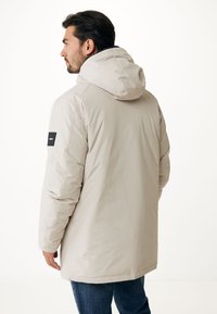 Beige parka bunda s kapucí, hladkým povrchem, elastickými manžetami a značkovou nášivkou na levém rukávu. Prodloužený zadní lem.