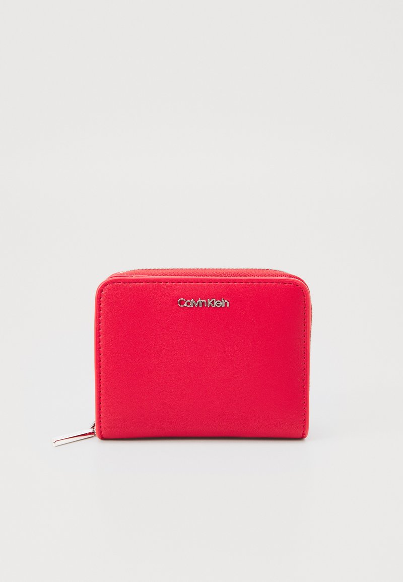 Red zippered wallet made of smooth synthetic material. Features a Calvin Klein logo on the front. Compact rectangular shape with a zipper pull.