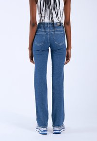 Jeans dritti blu con lavaggio medio, cuciture a contrasto, design a cinque tasche e etichetta con logo sul retro della vita.
