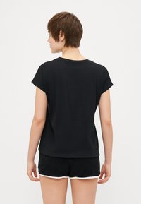 Melnas īsām piedurknēm T-krekliņš ar brīvu piegriezumu un apaļu kakla izgriezumu, izgatavots no mīksta auduma. Valkāts kopā ar melniem šortiem, kuriem ir baltas apmalītes.