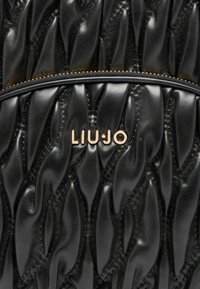 Sección de bolsa de cuero negro acolchado con textura fruncida, zipper dorado visible y logo de la marca "LIU JO" dorado centrado en la superficie.