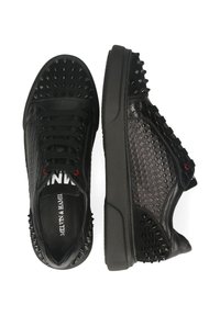 Schwarze Sneakers aus strukturiertem Leder, mit Pyramidennieten an der Spitze und an der Seite, schwarzen Schnürsenkeln und roten Akzenten auf der Zunge.