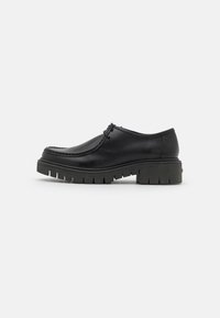 Zwarte lederen schoen met een ronde neus, gestikte details en een dikke, geribbelde rubberen zool. Heeft een minimalistisch vetersluiting ontwerp en een lage hak.