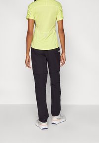 Krátké rukávy, jasně žlutý sportovní top s reflexními detaily, doplněný černými cargo kalhotami s nohavicemi na zip a bočními kapsami.