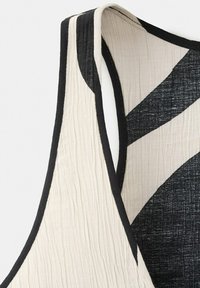 Maiou fără mâneci cu dungi diagonale alb-negru și margini subțiri negre pe zona brațelor și a gâtului.