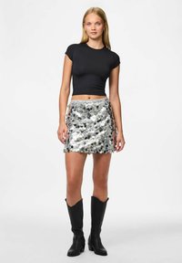 Zwarte aansluitende t-shirt gecombineerd met een glinsterende zilveren pailletten minirok, met een golvende rand en een elastische tailleband. Zwarte cowboylaarzen maken de look compleet.