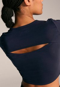 Haut de sport bleu marine à manches courtes, avec un détail découpé à l'arrière. Tissu lisse et extensible avec une coupe ajustée.