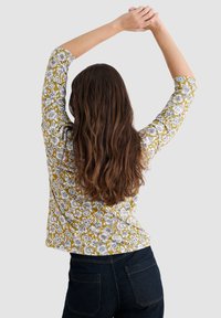 Maglia a maniche lunghe con sfondo giallo senape e motivi floreali bianchi. Design aderente con scollatura rotonda e leggera texture.