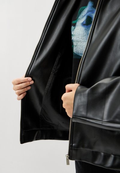 Black leather jacket with a smooth texture, featuring a zipper closure, and hands holding the open jacket to display the interior lining.