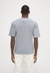 Camiseta de manga corta a rayas grises y blancas con cuello redondo, que presenta una textura suave y costuras visibles en los hombros.