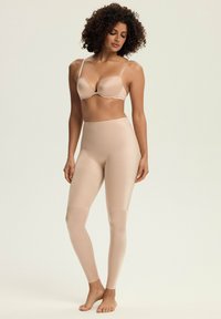 Beżowy bezszwowy biustonosz i zestaw legginsów z wysokim stanem, wykonany z gładkiego materiału, z cienkimi ramiączkami i dopasowanym krojem.