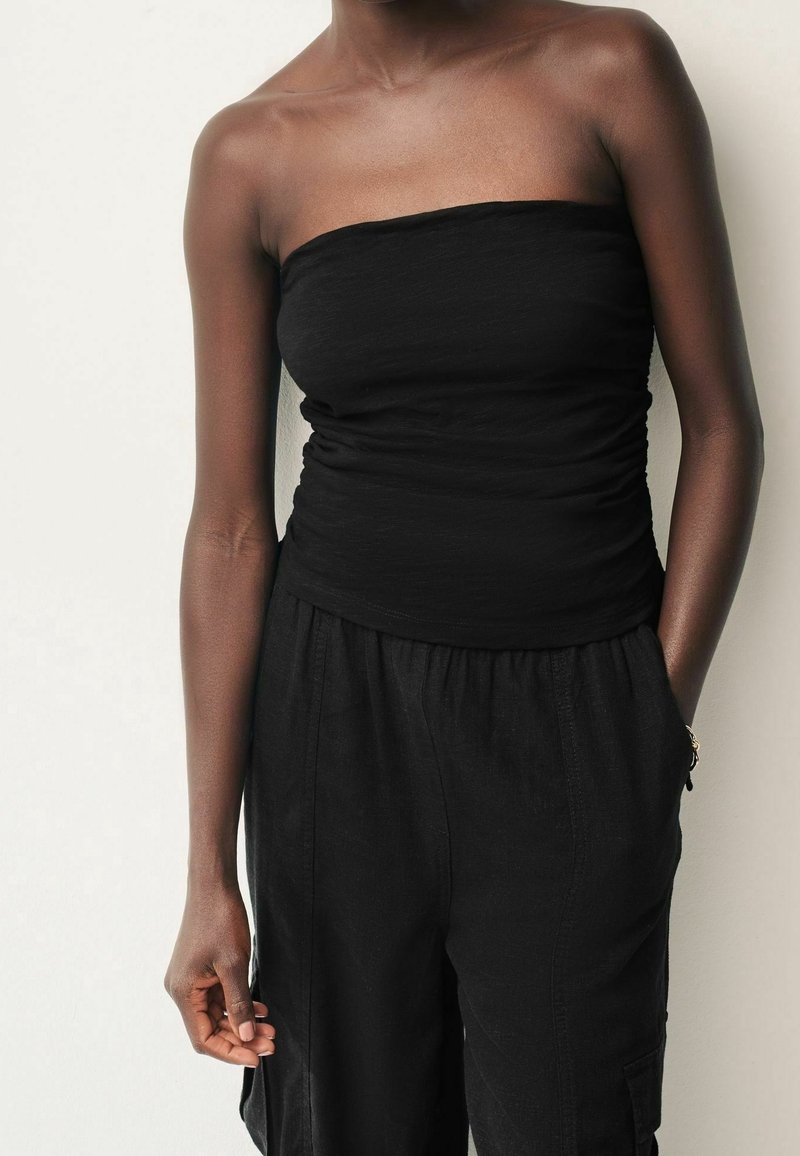 Top nero senza spalline con un design arricciato, realizzato in materiale leggero, abbinato a pantaloni neri larghi con tasche laterali.