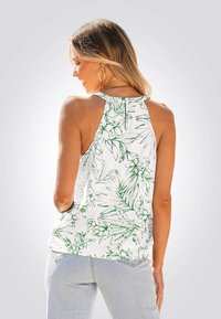 Top sin mangas blanco con patrón floral verde, diseño de cuello halter y cierre de un botón en la parte posterior, combinado con jeans de color azul claro.