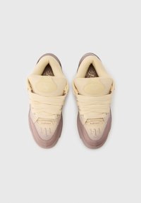 Ανοιχτό μπεζ αθλητικά παπούτσια με απαλή υφή. Διαθέτουν εμφανή κορδόνια, μαξιλαρωμένη γλώσσα και καφέ λαστιχένια σόλα. Τα διακοσμητικά στοιχεία περιλαμβάνουν λογότυπα και ραφές.