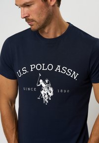 Marineblå kortermet T-skjorte laget av bomull, med en hvit grafikk av to polo-spillere og teksten "U.S. POLO ASSN. SINCE 1890."
