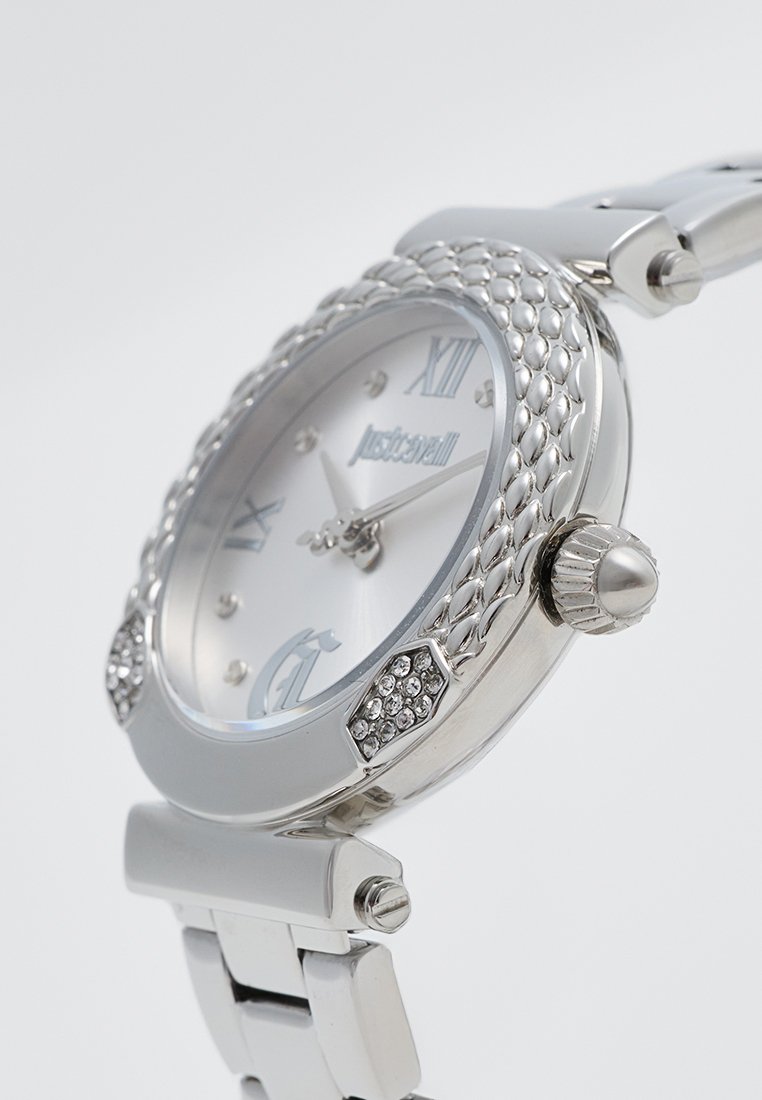 Orologio argento con cassa rotonda, lunetta texturizzata, quadrante bianco, numeri romani e accenti in cristallo. Dotato di bracciale in metallo a maglie.