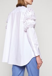 Witte blouse met opgeblazen, getextureerde mouwen in een gerimpeld ontwerp. Losse pasvorm, gebogen zoom en met knopen afgewerkte manchetten van een gladde stof.