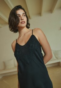 Fekete selyem camisole, hímzett csipke részletekkel a dekoltázsnál, állítható pántokkal és sima, áramló kialakítással.