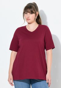 T-shirt bordeaux a maniche corte e scollo a V realizzato in tessuto morbido, con una vestibilità comoda e orlo leggermente curvato, abbinato a jeans blu.