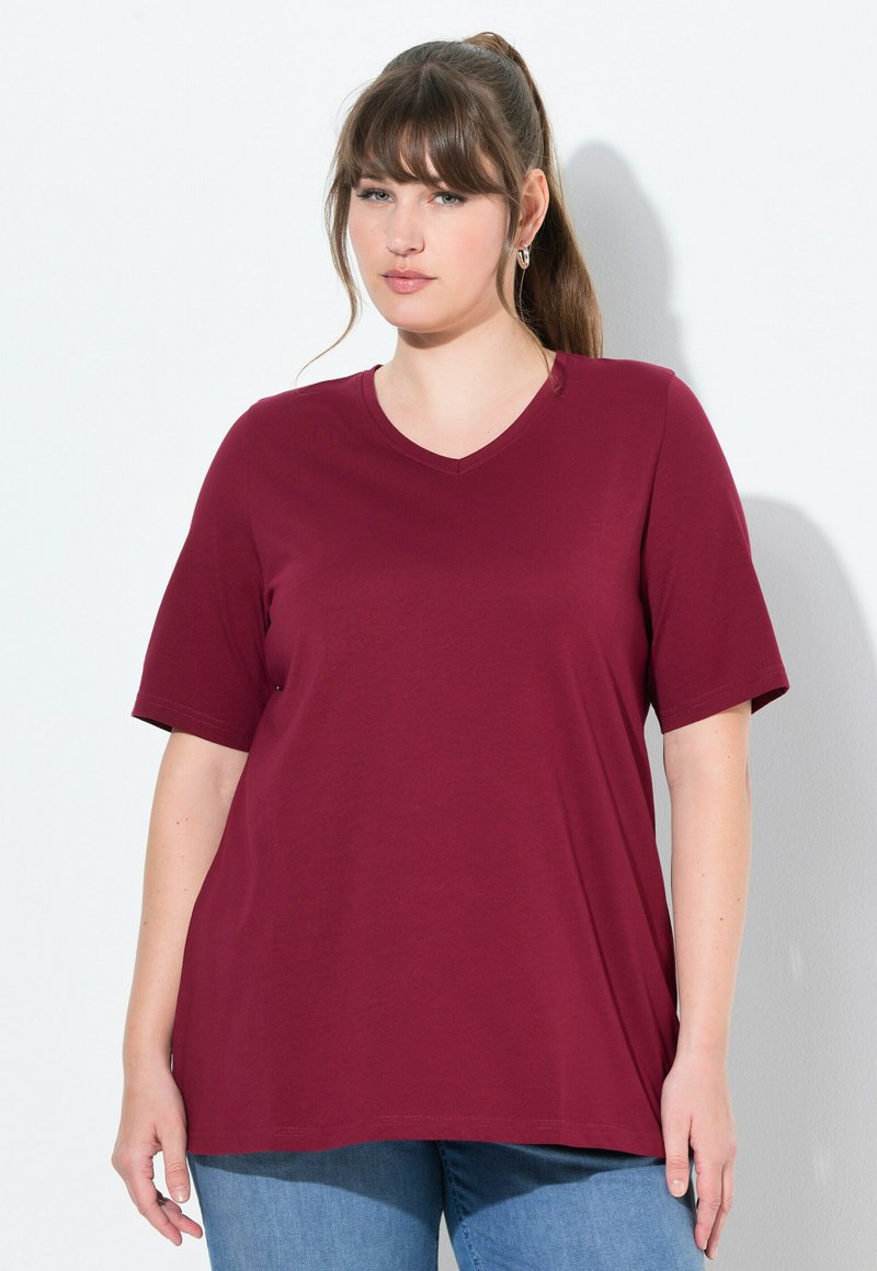 T-shirt bordeaux a maniche corte e scollo a V realizzato in tessuto morbido, con una vestibilità comoda e orlo leggermente curvato, abbinato a jeans blu.