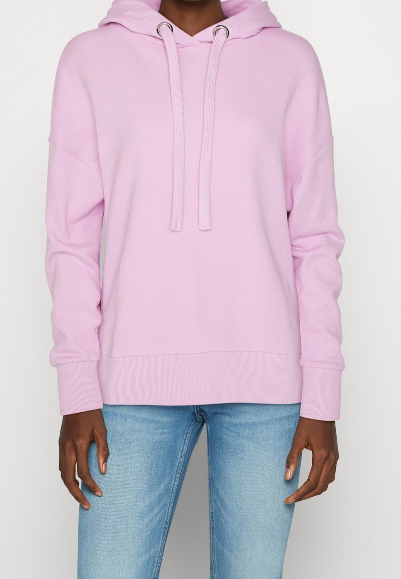 Light pink hoodie made of soft fabric, featuring a drawstring hood, ribbed cuffs, and a relaxed fit. Paired with light blue jeans.