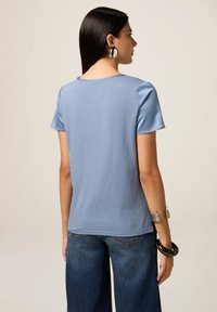 Top de culoare albastră cu mânecă scurtă, dintr-un material moale, având un decolteu rotund și o croială lejeră, asortat cu pantaloni din denim cu picior larg.