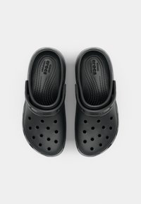 Paire de sabots Crocs noirs avec trous de ventilation et brides au talon, positionnée debout sur un fond clair uni.