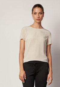 Beige kortärmad blus i lätt material med rund halsringning, matchad med figurnära svarta byxor. Slät textur, klassisk design.