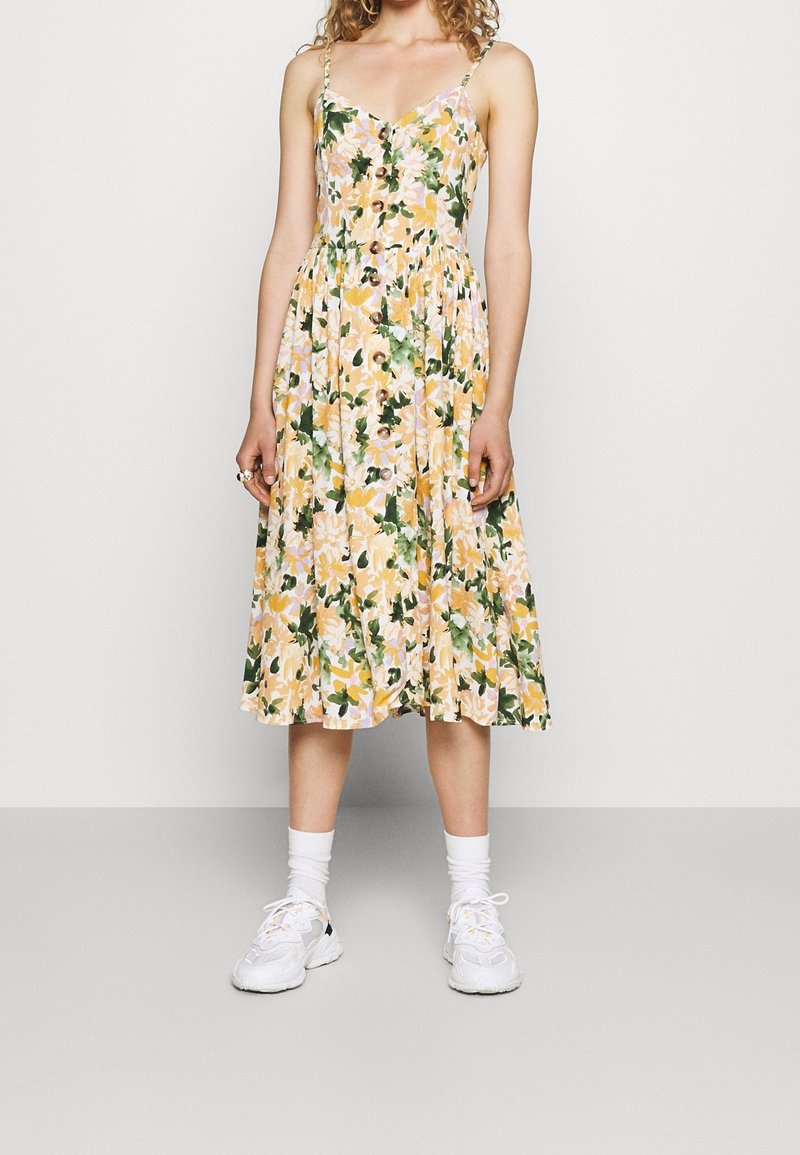 Vestido midi floral con un estampado en amarillo, rosa y verde, escote en V, botones en la parte delantera y tirantes ajustables.