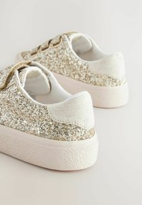 Baskets recouvertes de paillettes dorées, avec un talon blanc texturé et une doublure intérieure douce, dotées d'un bout rond et d'une semelle en caoutchouc rose.