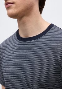 Κοντινό πλάνο ενός ατόμου που φοράει μπλε ναυτικό και λευκό λεπτό ριγωτό μπλουζάκι με στρογγυλή λαιμόκοψη, εμφανίζοντας το κάτω μέρος του προσώπου, τον λαιμό και το πάνω μέρος του στήθους.