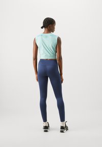 Gaiši zils bezpiedurkņu tops ar īsāku dizainu, apvienots ar augstā vidukļa tumši zilām legingām. Iezīmē Nike zīmolu un gludu tekstūru.