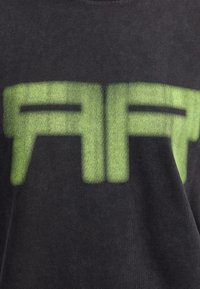 Μαύρο T-shirt με έντονο, πράσινο γραφικό κείμενο που γράφει "ART". Το ύφασμα φαίνεται απαλό με μια ελαφριά υφή.