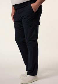 Námořnické cargo kalhoty mají uvolněný střih, mnoho kapes a hladkou texturu. Jsou kombinovány s bílými sportovními botami.