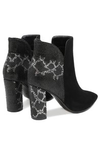 Botines negros con punta afilada, parte frontal de ante y parte trasera texturizada con un patrón de piel de serpiente, sostenidos por un tacón grueso.