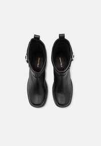 Bottines en cuir noir à bouts carrés, avec des brides latérales à boucles argentées et des languettes à l'arrière, vues de dessus sur fond blanc.