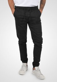 Black jogger pants made of lightweight fabric with an elastic waistband, drawstring, and cuffed ankles, featuring side pockets and stitching details.