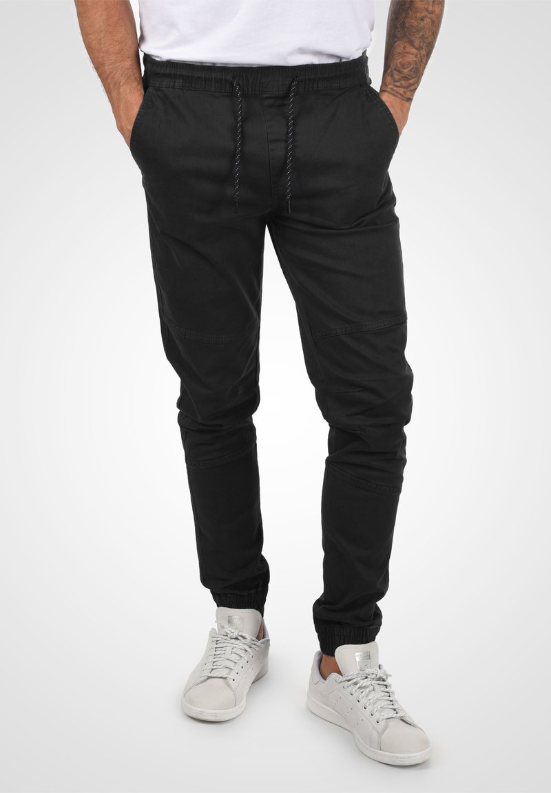 Black jogger pants made of lightweight fabric with an elastic waistband, drawstring, and cuffed ankles, featuring side pockets and stitching details.