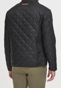 Veste matelassée noire avec une finition texturée, dotée d'un accent en cuir marron sur le col, conçue avec une coupe moderne et des poches latérales.