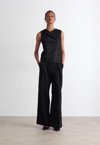 Melnas bezpiedurkņu blūze ar plūstošu dekoltē, apvienota ar plašiem melniem biksēm. Gluda auduma, minimālisma dizaina un bez redzamām rakstu. 