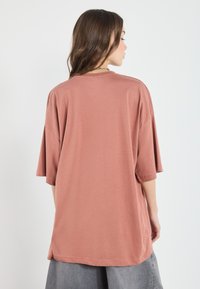 Overdimensioneret, kortærmet t-shirt i støvet rosa farve, lavet af blødt stof med en glat tekstur og rund halsudskæring.