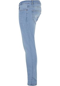 Jean en denim bleu clair avec une coupe slim, présentant des détails d'usure subtils à l'avant, un design classique à cinq poches, et une ceinture standard.